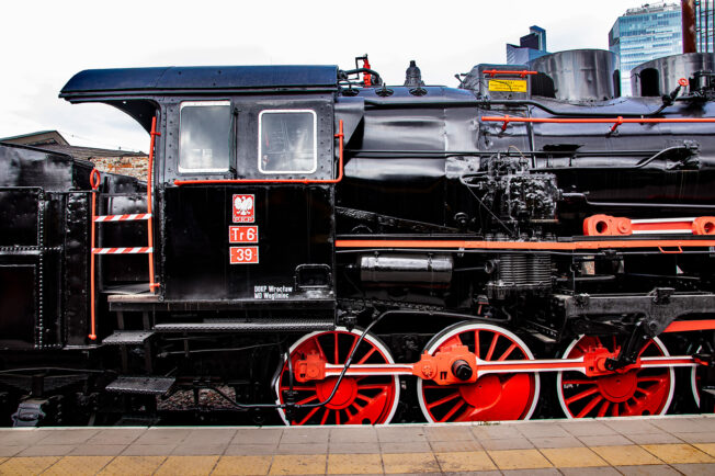 Czarna lokomotywa parowa oznaczona numerem Tr6-39 stoi na torach kolejowych, eksponując czerwone koła i części konstrukcyjne. Kabina maszynisty jest zamknięta, a na bocznej ścianie widoczny jest herb Polski. Lokomotywa z dobrze widocznym zestawem kół parowozowych oraz różnego rodzaju rurami i mechanizmami jest zadbana i odrestaurowana.