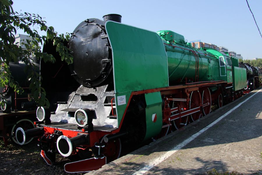 Zielono-czarna lokomotywa parowa z okresu powojennego eksponowana jest na zewnątrz na torach kolejowych. Środkowa część ciężkiego pojazdu wyposażona jest w liczne skomplikowane elementy mechaniczne, z charakterystycznym, wielkim kotłem parowym i cylindrami. Lokomotywa ma czerwone obręcze kół oraz czarną, zaokrągloną przednią część z reflektorem.