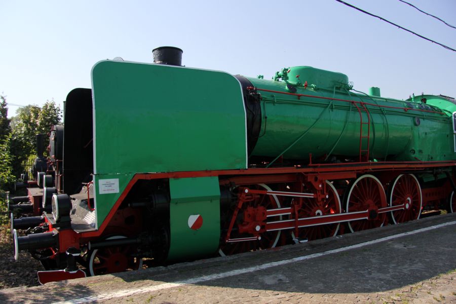 Lokomotywa parowa Pt47-104 o zielonym kolorze z dużymi czerwonymi kołami stoi na torach kolejowych. Widać zakrzywiony komin i charakterystyczne nity na zbiorniku parowym. Po jej bokach umieszczono białe oznaczenia.