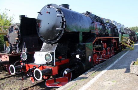 The steam locomotive with the designation Ty43-17 stands on the tracks; its body is black with red wheel rims and accents. The locomotive is equipped with a large, round front boiler and has black, horizontal pipes running along the side of the body. Metal steps and platforms are visible on the sides, which facilitate access to the interior of the machine.