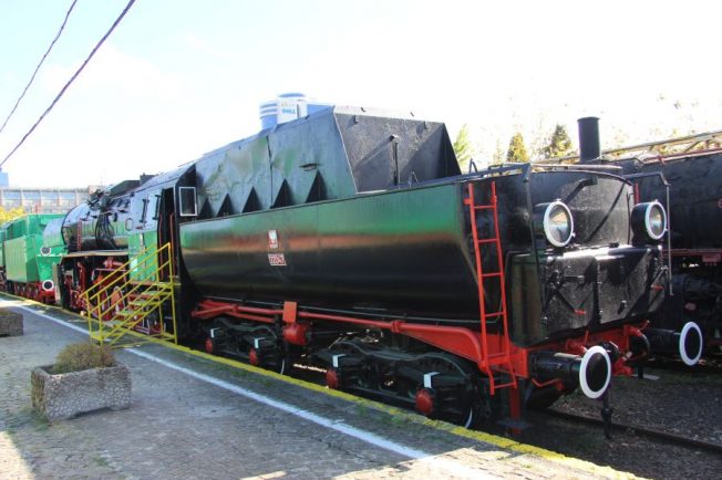 Czarno-zielona lokomotywa parowa z czerwonymi elementami stoi na torach; to model Ty43-17 z okresu powojennego. Posiada charakterystyczną budowę z dużym kotłem i kabiną dla załogi na końcu. Przed lokomotywą widoczne są także inne wagony w tle.