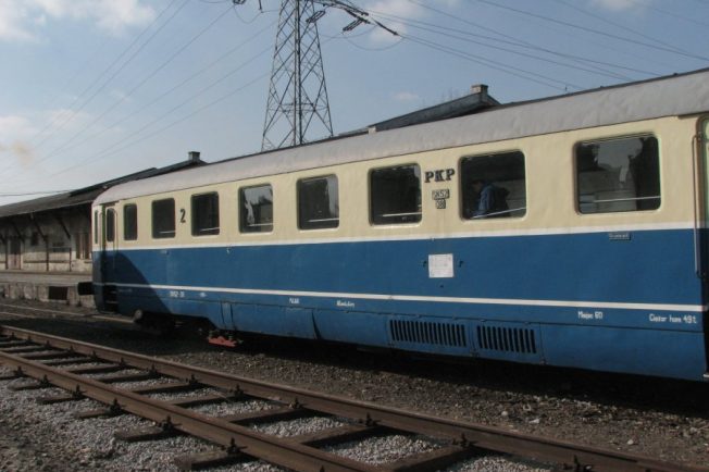 Niebiesko-biały wagon motorowy stoi na torach kolejowych. Ma napis 