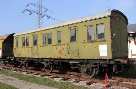 Wagon pasażerski o konstrukcji drewnianej stoi na torach, jego malowanie to odcienie zieleni. Wyposażony jest w dwa zestawy kołowe i ma drzwi umieszczone przy jednym z końców. Dach wagonu jest zaokrąglony, posiadają okna i są oznaczone czerwonymi światłami.