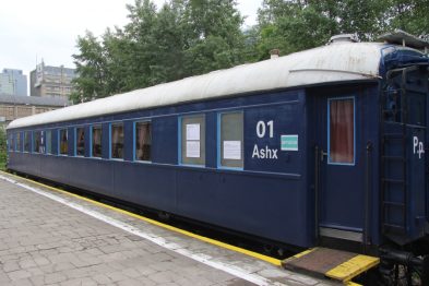 Niebieski wagon kolejowy stoi na peronie, jego boczne ściany są ozdobione tablicami informacyjnymi oraz numerem 