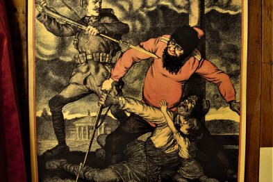 Plakat z grafiką przedstawia postać żołnierza w mundurze z czasów wojny trzymającego sztandar, za nim rozpościera się wschodzące słońce. Pod grafiką widnieje napis 