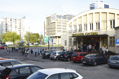 Ludzie stoją w kolejce przed wejściem do budynku z napisem 