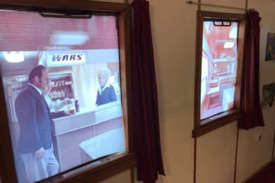 Wagon pasażerski jest wyposażony w drewniane okna, przez które widać rozmowę dwóch osób w wagonie restauracyjnym na ekranie telewizora zawieszonego na ścianie; nad telewizorem widoczny jest napis „WARS”. Po prawej stronie telewizora znajduje się drzwi z szybą, a obok okna zawieszone są czerwone, wzorzyste zasłony. Ściany wagonu są obite drewnianą boazerią, a przestrzeń jest oświetlona ciepłym, żół