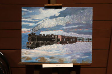 Obraz przedstawia parowóz ciągnący skład wagonów na tle zachmurzonego nieba, z którego wydobywa się bujny dym komina lokomotywy. Skład porusza się przez pokrytą śniegiem ziemię, podkreślając zimową aurę. Malowidło wyróżnia się żywą kolorystyką z dominującym błękitem nieba i bielą śniegu.