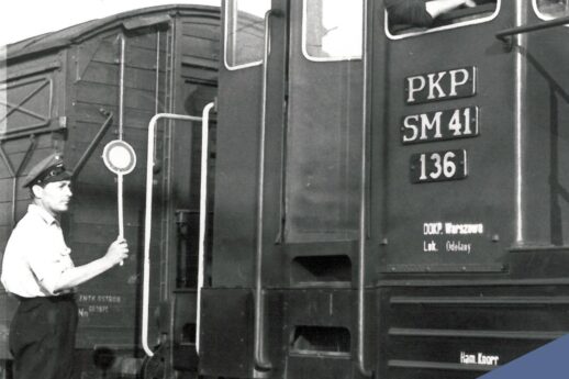 Mężczyzna w mundurze z czapką daje sygnał lizakowym semaforem do osoby wychylającej się z okna pociągu. Obok stoi wagon kolejowy z oznaczeniem PKP i numerem SM41 136. W tle widoczna jest kolejna część składu pociągu.