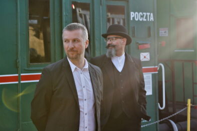 Dwóch mężczyzn stoi przed zielonym wagonem kolejowym z napisem 