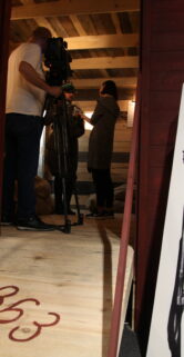 Osoba w historycznym mundurze została przedstawiona na stojącym plakacie, który jest ustawiony przy wejściu do wagonu kolejowego. Czeladź obsługująca kamerę filmuje wewnątrz wagonu, gdzie dokonuje się jakaś aktywność. Podłoga przed wagonem jest oznaczona rokiem „1863”, który odnosi się do daty Powstania Styczniowego.