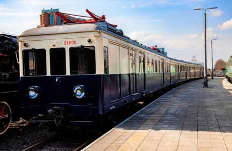 The electric train is standing on the platform ready to depart. The vehicle has a classic paint scheme in shades of blue and cream typical for the era. Also visible are the pantographs on the roof, as well as the headlights and characteristic windows.