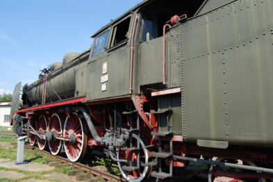 Starannie zachowana, zielona lokomotywa parowa Pt31 stoi na torach; otaczają ją trawiaste tereny. Posiada charakterystyczne, dużych rozmiarów czerwone koła oraz czarne elementy, takie jak komin. Maszyna jest wyposażona w liczne rury, okna kabiny oraz metalowe stopnie boczne.