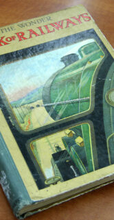 Starsza książka o kolejnictwie leży na płaskiej powierzchni. Okładka książki jest w kolorach zielonym i czarnym, z ilustracją parowozu. Tytuł na okładce brzmi "The Observer's Book of Railways".