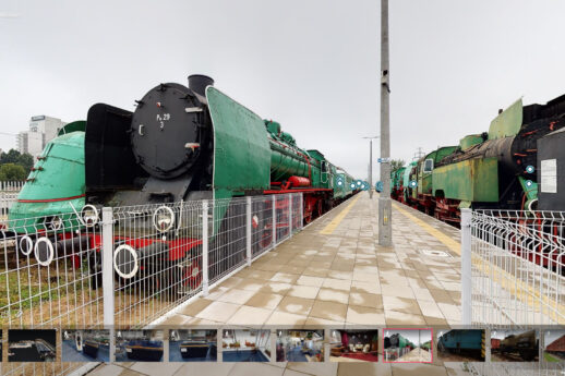 Zdjęcie przedstawia zewnętrzne ekspozycje kolejowe z szeregiem lokomotyw parowych umieszczonych na torach. Lokomotywy mają różne malowania i są skierowane frontem w kierunku obserwatora. Widoczna jest również metalowa ogrodzenie oraz kamienna nawierzchnia peronu.