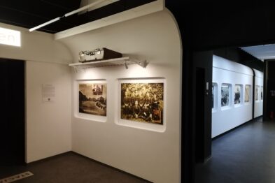 Eksponowane są fotografie związane z tematyką kolejową, umieszczone w białych ramach i oświetlone lampami na ścianie galerii. W prawej części widoczna jest kolejna galeria z wystawionymi fotografiami i informacjami tekstowymi obok nich. Przestrzeń wystawiennicza jest czysta i nowocześnie zaaranżowana z wyraźnymi ścieżkami dla zwiedzających.