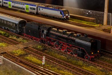 Detalowana makieta kolejowa przedstawia parowóz z wagonami na torach obok peronu; w tle widoczny jest współczesny skład pasażerski. Modele są starannie wykonane z dbałością o detale, zarówno lokomotywa, jak i wagony posiadają liczne detale konstrukcyjne. Oświetlenie makietowe podkreśla realistyczny charakter sceny, imitując nocne warunki oświetleniowe.