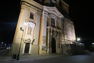 Budynek teatru im. Andreasa Gryphiusa w Głogowie jest oświetlony w nocy. Barokowa fasada świątyni z dwoma rzeźbami umieszczonymi w niszach zdobi fronton. Teatr stoi przy pustej ulicy wyłożonej kostką brukową.