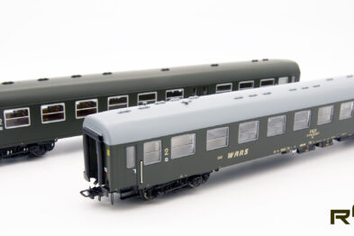 Dwa modele wagonów pasażerskich stoją obok siebie na białym tle. Modele mają zielono-szarą kolorystykę z widocznymi oknami i drzwiami. Na boku każdego modelu znajduje się logo ROBO Modele.