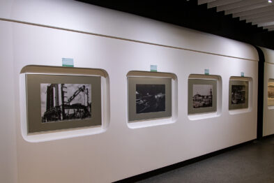 Ściana w galerii pokryta jest serią oprawionych fotografii związanych z tematyką kolejnictwa. Każdy z czarno-białych obrazów jest oświetlony pojedynczym reflektorem i zawiera różne sceny przedstawiające pociągi oraz kolejowe otoczenie. Fotografie są zawieszone w równych odstępach i prezentują się jako elegancki zbiór dzieł sztuki.