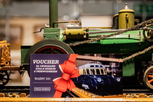 Kolorowa kartka (voucher) oparta o model starego parowozu na regale w sali wystawowej