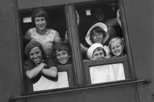 Zdjęcie czarno-białe. Uśmiechnięte dzieci wyglądają przez okno wagonu kolejowego.
