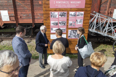 Grupa osób przed wagonem towarowym, który jest scenerią wystawy