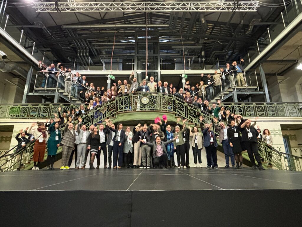 Zdjęcie grupowe z około setką osób na konferencji. Zdjęcie pozowane.