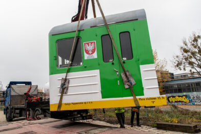 Odcięta kabina pociągu zielono-biało-żółta jest podnoszona podnośnikiem i zdejmowana z lawety i stawiana na peronie