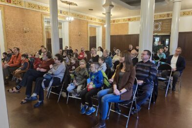 Widzowie siedzący na krzesłach na sali, słuchają wykładu prelegenta