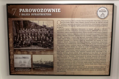 Plansza wystawowa upamiętniająca 140-lecie Drogi Żelaznej Iwangrodzko-Dąbrowskiej, znajdująca się w Stacji Muzeum. W tle historyczne zdjęcie kolejarzy. Tytuł planszy: „Parowozownie