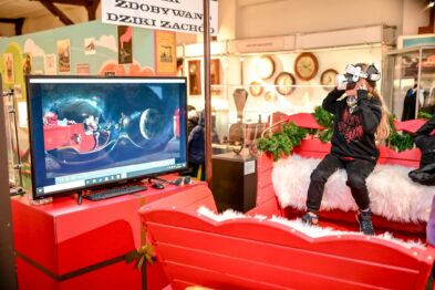 Dziecko w goglach vr na głowie siedzi w saniach obok telewizor