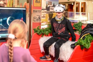 Dziecko w goglach vr na głowie siedzi w saniach obok telewizor