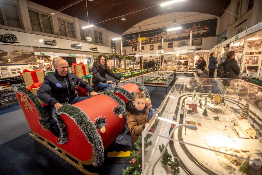 Zwiedzający w saniach św. Mikołaja przy makiecie kolejowej