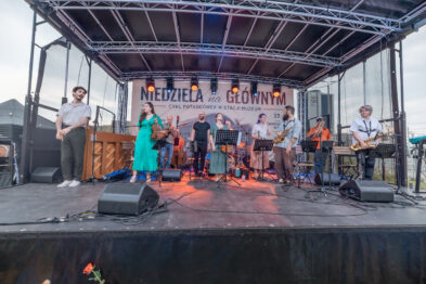 Muzycy zespołu Mała Orkiestra Dancingowa stoją na scenie po zakończonym utworze. W tle widoczny jest baner „Niedziela na Głównym”.